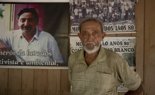A person wears a brown shirt and stands next to a portrait photo.