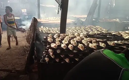 People work inside a tent with fish stacked up to dry