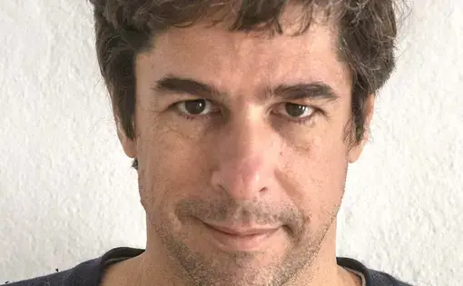 A man with short brown hair, a black sweater and grey shirt.