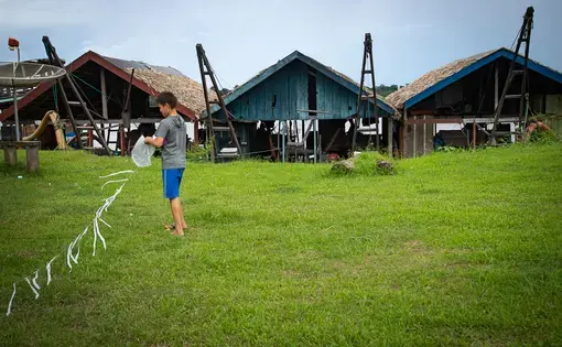 A boy playing with a kite, in the background the mining rafts anchored on the banks of the Madeira River