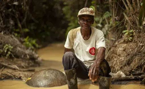 Un hombre al lado de un rio con sus herramientas para extraer oro