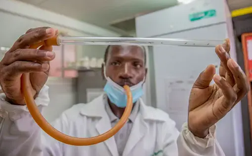 A scientist holds a glass tube of mosquitoes between his two index fingers.