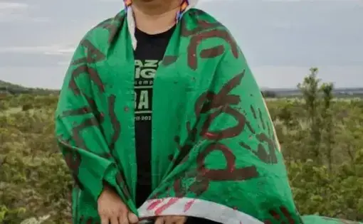 An indigenous woman stands smiling and gazing proudly in her traditional attire.