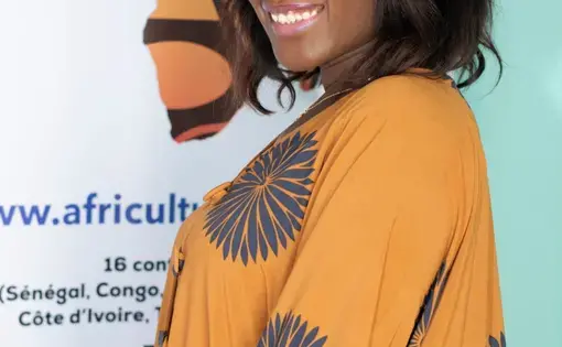 A woman smiles clad in a mustard dress against a flex standee with a map of Africa on it.