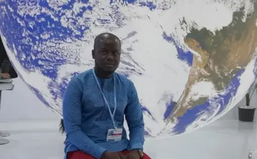 A man sits atop a stool against a life-size, giant globe.