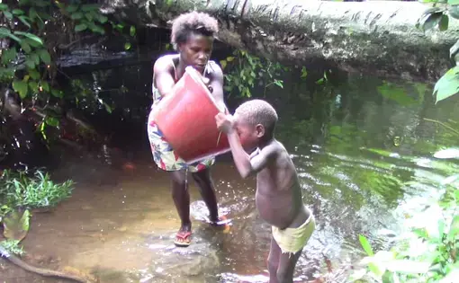 a child drinking water from a tub in her mother's hands.