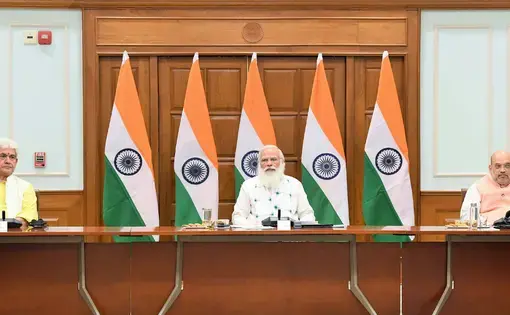 Modi sits at a table with Indian flags in the background