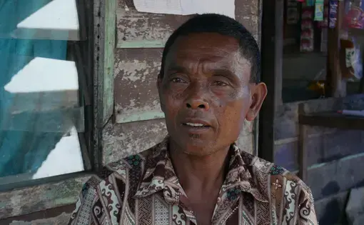 A man wearing a brown, printed shirt sitting on a chair.