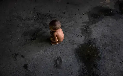 A child crouches on the wide black, floor.
