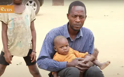 a baby wearing an orange t-shirt is cradled in his father's arms.