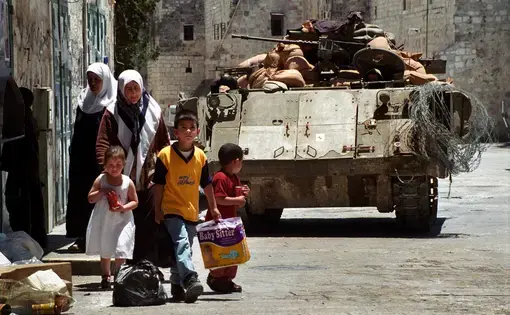 BETHLEHEM, PALESTINIAN AREAS - MAY 28: Palestinian residents of Bethlehem walk near an Israeli tank guarding Manger Square during a lull in curfew imposed by the Israeli military May 28, 2002 in Bethlehem. Image by Ryan Rodrick Beiler/Shutterstock.