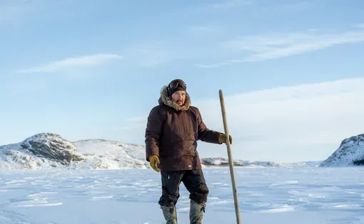A man holding a long tool stands in an icy field.