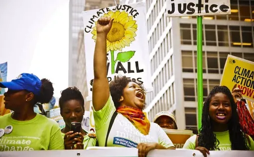 A group of Black women stand smile and march with banners reading "Climate Action Now" and "Climate Justice for All"