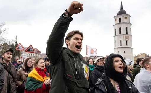 a man holds his fist high and yells in protest among others in an outdoor setting