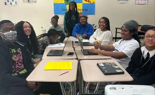 Students pose for a photo at their classroom desks