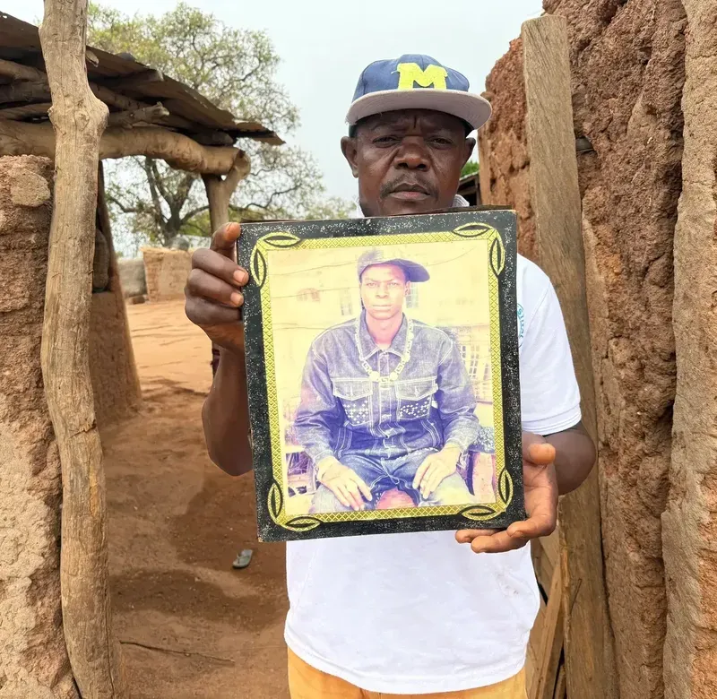 a man holds up a framed picture of another person