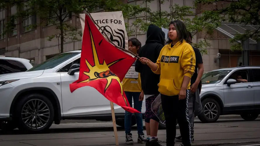 Jenae Turtle looks back at the marchers behind her, waving a Mohawk Warrior Flag often used to&nbsp;represent unity among Indigenous people.&nbsp;Canada, 2019. Image by Shelby Gilson.