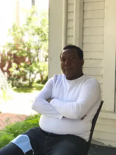 Panbo Boris sitting on the porch of his home in Yarmouth. Image by Francesca Bentley. United States, 2020.&nbsp;