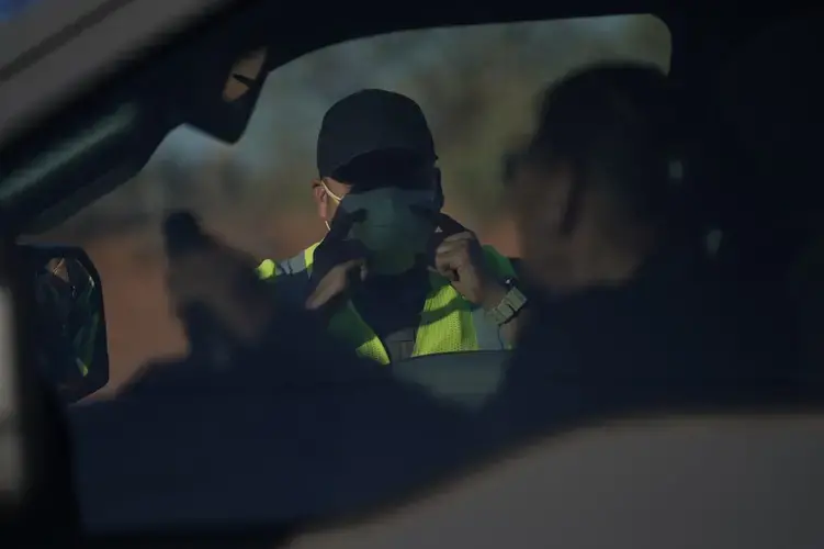 An officer with the Navajo Nation Police talks to a driver at a roadblock in Tuba City, Ariz., on the Navajo reservation on April 22, 2020. The roadblock was to inform residents of evening and weekend curfews, hand washing, and wearing a face mask to help control the spread of COVID-19. Image by AP Photo/Carolyn Kaster. United States, 2020.