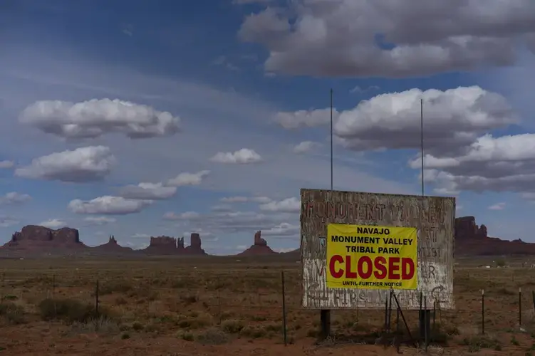 A sign reads 'Navajo Monument Vally Tribal Park Closed Until Further Notice' posted at the entrance of Monument Valley in Oljato-Monument Valley, Utah, on the Navajo reservation April 19, 2020. The reservation has some of the highest rates of coronavirus in the country. If Navajos are susceptible to the virus' spread in part because they are so closely knit, that's also how many believe they will beat it. Image by AP Photo/Carolyn Kaster. United States, 2020.