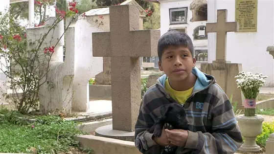 Benjamin Obando, 11, prays and sings at a cemetery in Cochabamba, earning about $3 per day. 'I bring money home for my family, to give them food,' he said. Image by Tracey Eaton. Bolivia, 2017.