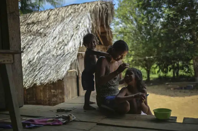 A Timbo Indian mother smiles as she does her six-year-old daughter's hair. Her second son plays behind her. Image by Luis Ángel. Colombia, 2019.