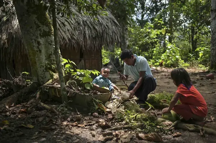 A father cuts up a coconut to share with his two small children. Image by Luis Ángel. Colombia, 2019.