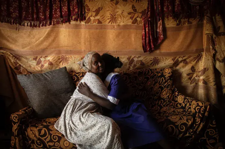 Dorcas Choya sits with Susie on her couch, who fled her home when her parents brought a circumciser to cut her. “When I saw her I just ran,” said Susie. “I didn’t bother taking anything. I ran without shoes.'&nbsp;Image by Will Swanson. Kenya, 2020.
