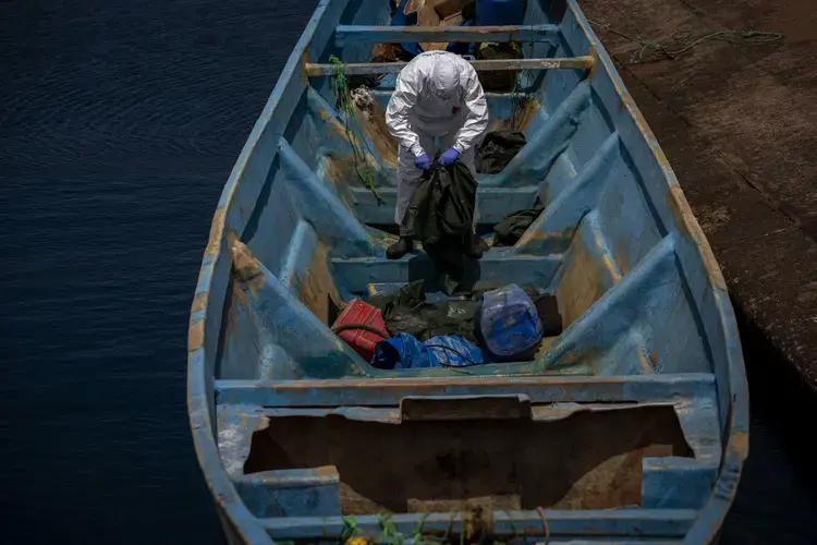 A police officer inspects a boat where 15 Malians were found dead adrift in the Atlantic on Thursday, Aug. 20, 2020, in Gran Canaria island, Spain.&nbsp;Image by Emilio Morenatti/AP Photo. Spain, 2020.