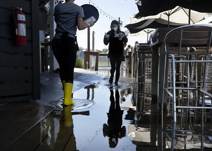 Servers Alexandra Schroettner and Christi Hughes wade through salt water that has risen over the patio at Saltwater Cowboys as they serve guests lunch on Shem Creek on Monday, Sept. 21, 2020, in Mount Pleasant. Image by Grace Beahm Alford /&nbsp;Post and Courier. United States, 2020.