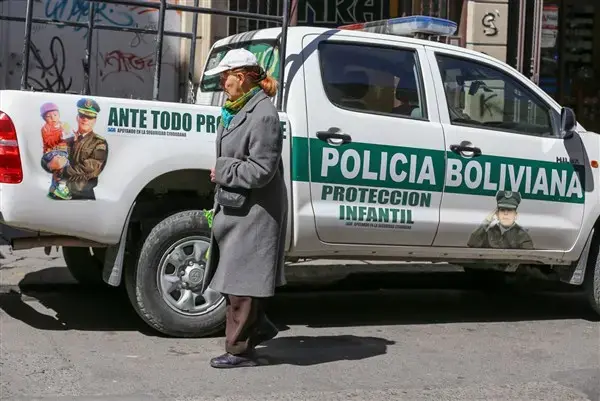 A woman walks past a police truck marked 'child protection' in La Paz, where a 2014 law allows children to work as young as age 10. Government supporters say the law protects children and gives them a voice. Image by Tracey Eaton. Bolivia, 2017.