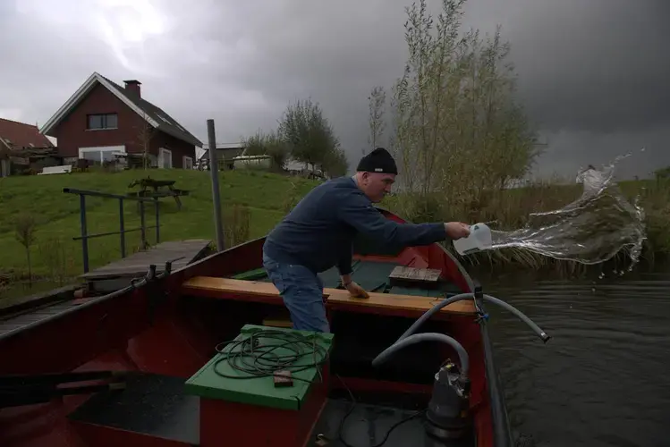 Vic Gremmer bails out his wooden boat before a rain storm in South Holland. Gremmer agreed to relocate his home as part of a program that makes room for for rivers to flood safely. Image by Chris Granger / Times-Picayune / The Advocate. Netherlands, undated.<br />
