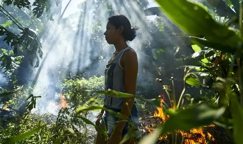 Joane beside a bonfire used to burn plastic waste. Image by Pablo Albarenga. Brazil, 2019.