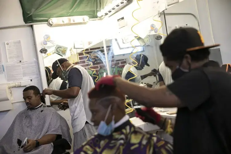 Geoffrey West, 34, second left, cuts the hair of customer Bayione Rogers, 22, at the Court Barbershop in Athens, Ohio. Image by Wong Maye-E/AP Photo. United States, 2020.