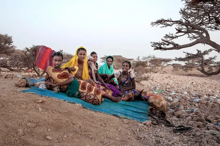 In this July 15, 2019 photo, Ethiopian Tigray teen migrants rest under a tree on the last stop of their journey before leaving by boat to Yemen in the evening, in Obock, Djibouti. An increasing number of the travelers include women and girls, who face rape and torture at the hands of human traffickers. Image by Nariman El-Mofty / AP Photo. Djibouti, 2019.