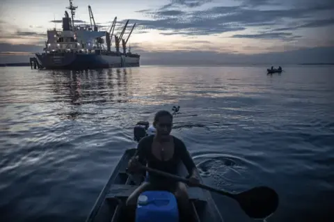 A woman on a tiny boat and a big cargo ship in the background