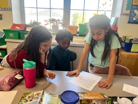 three young students examine worksheet on table