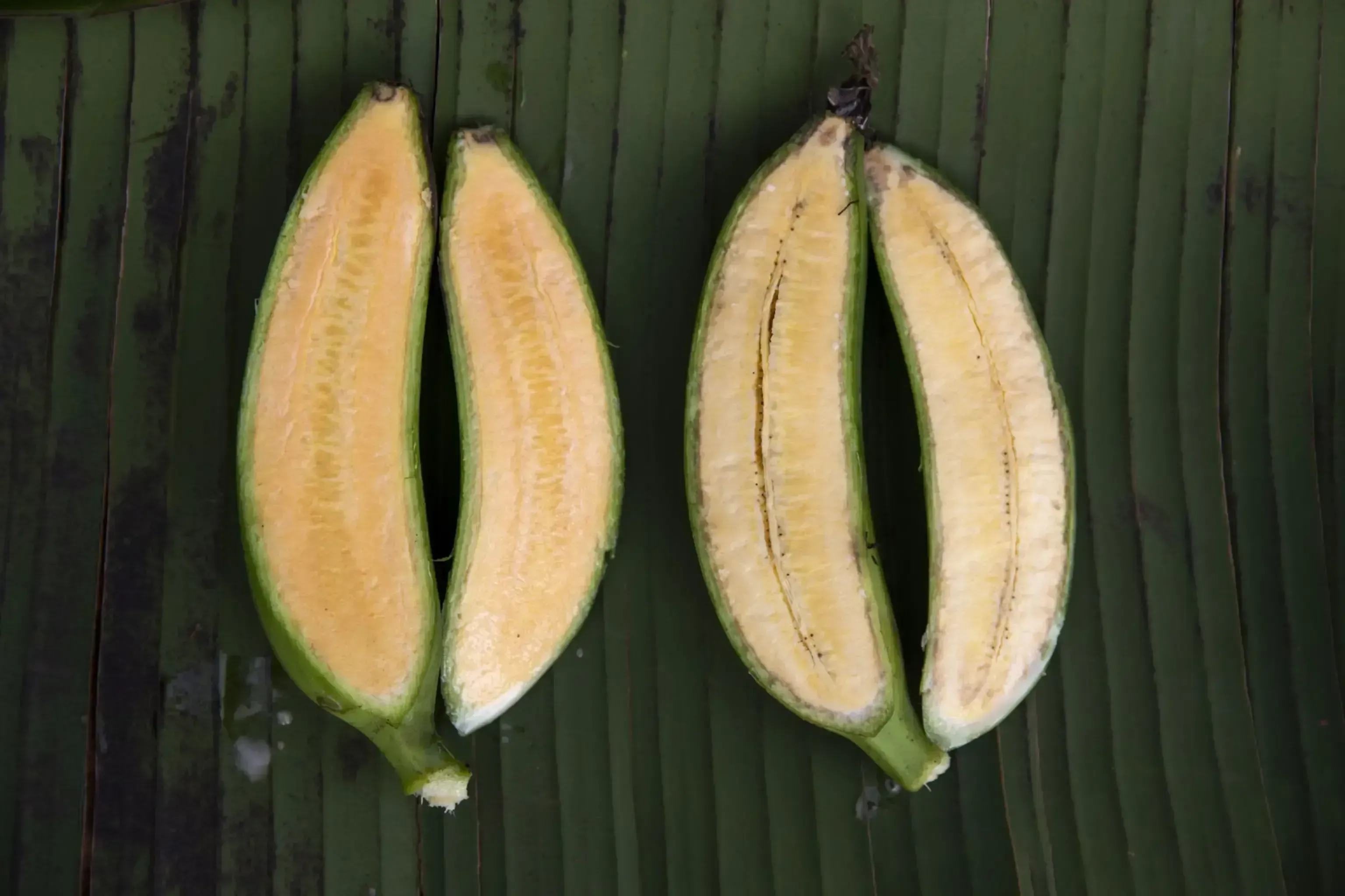 two bananas, cut lengthwise, sit on a green leaf