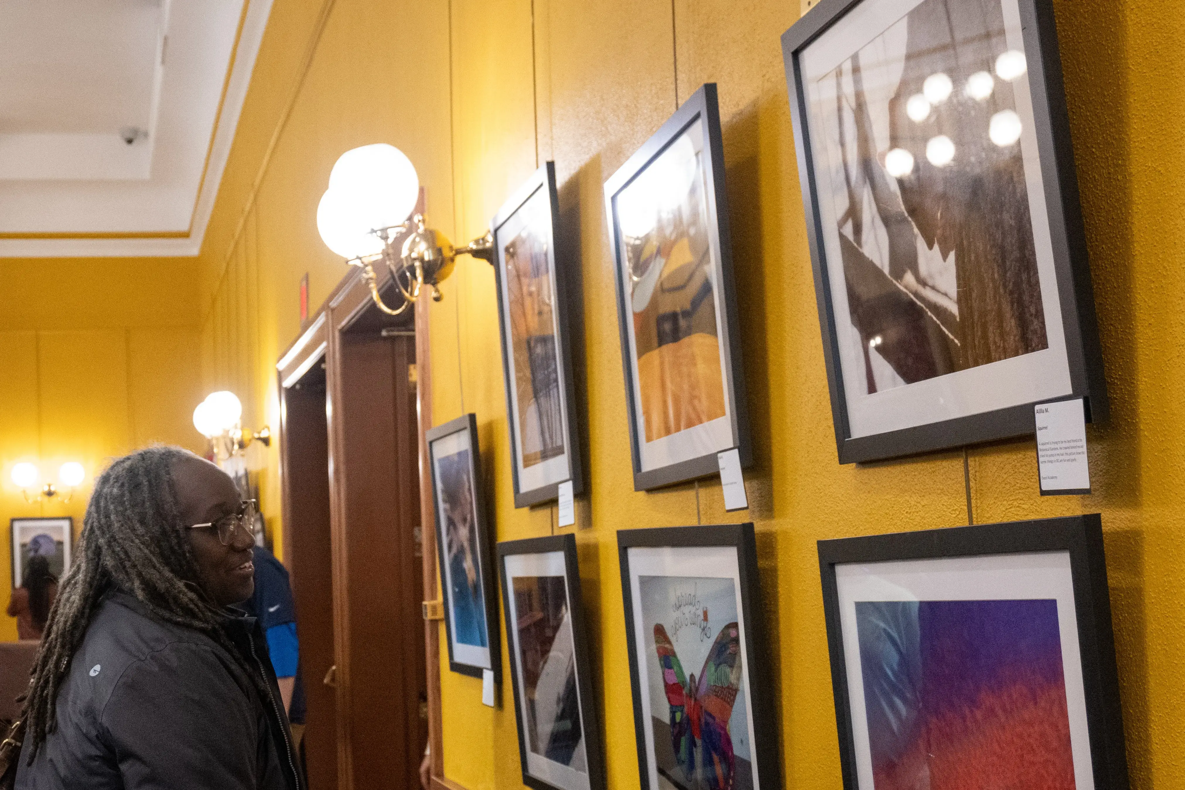 A woman with a blue jacket and braids looks at a wall of framed photos in the Everyday DC gallery