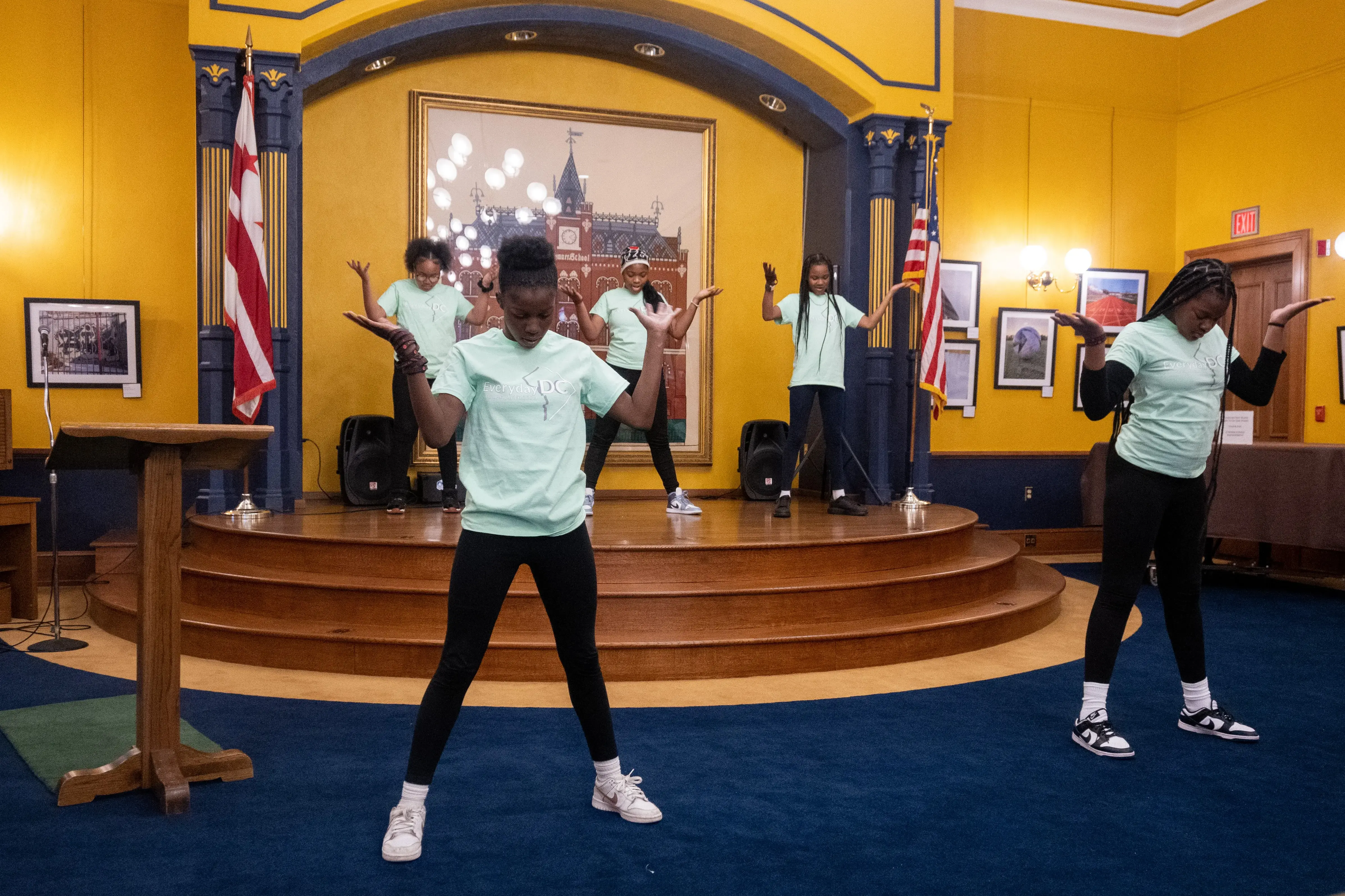 Six middle school students wearing green Everyday DC shirts pose during a dance in front of the audience for the Everyday DC opening reception