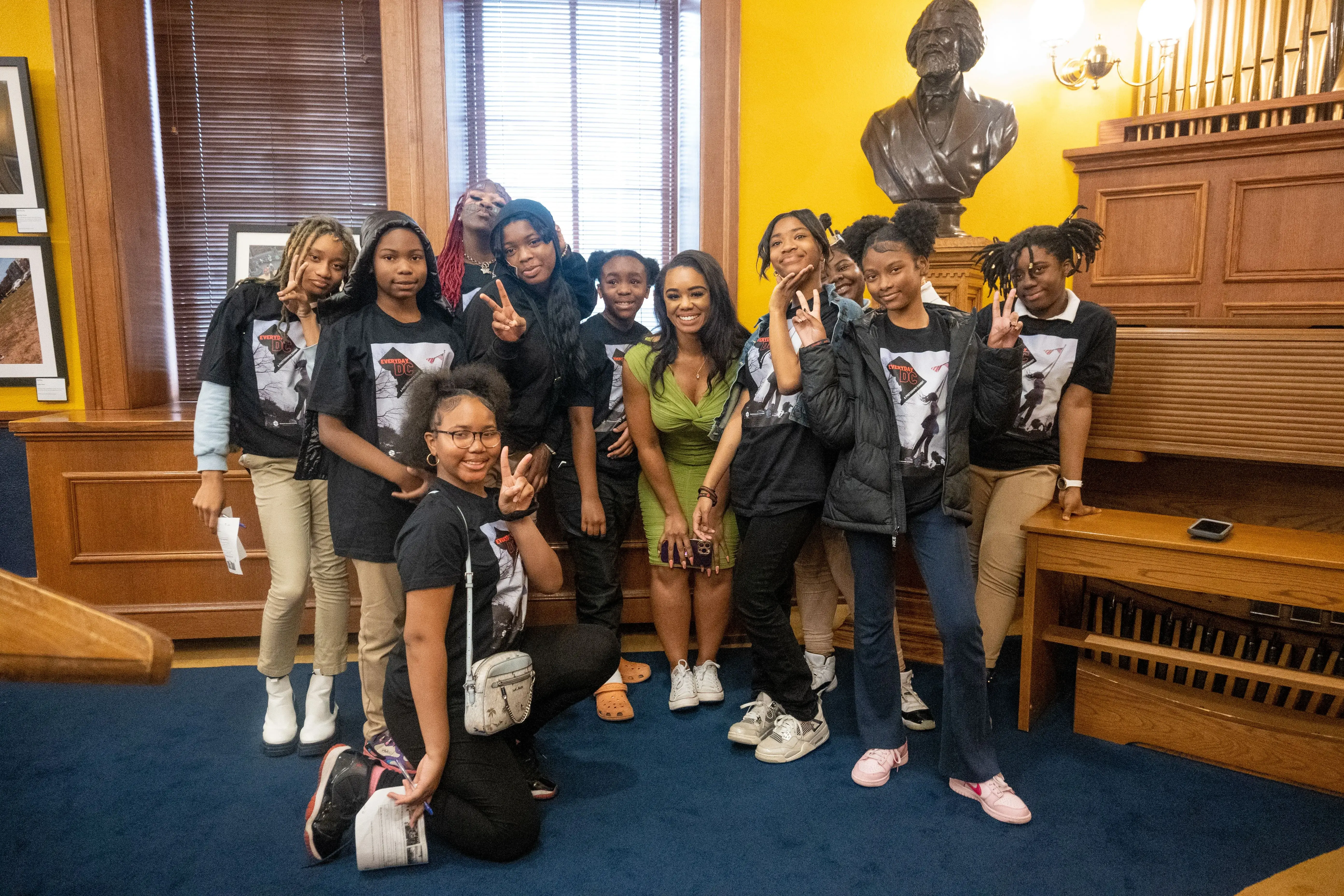 Students in black t-shirts from Excel Academy pose with journalist Ashonti Ford following her keynote speech at the Everyday DC student symposium at the Charles Sumner Museum and Archives in Washington, D.C