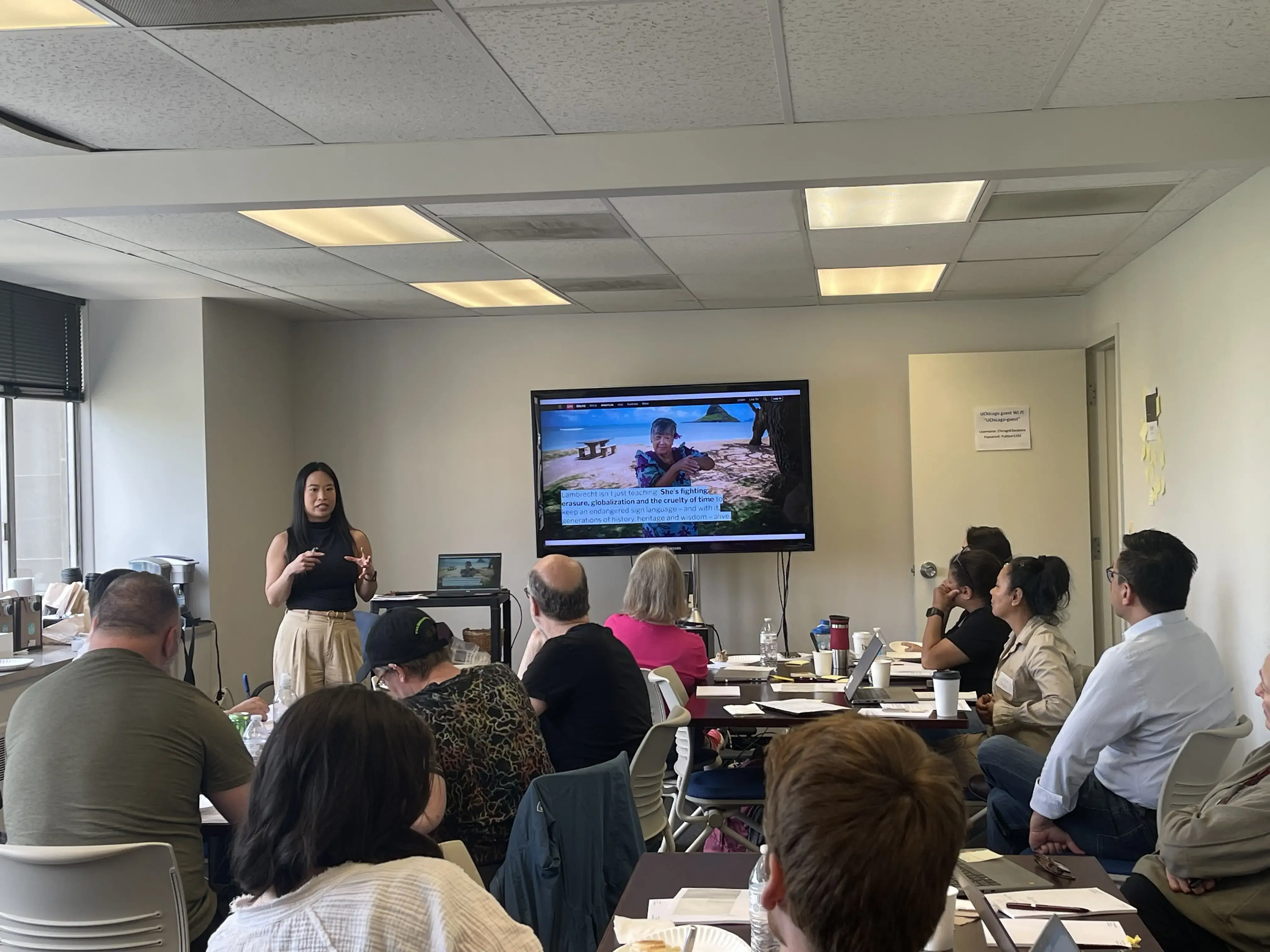 Journalist Corinne Chin speaks presents a photo on a screen and speaks to 20 educators who are seated and listening.
