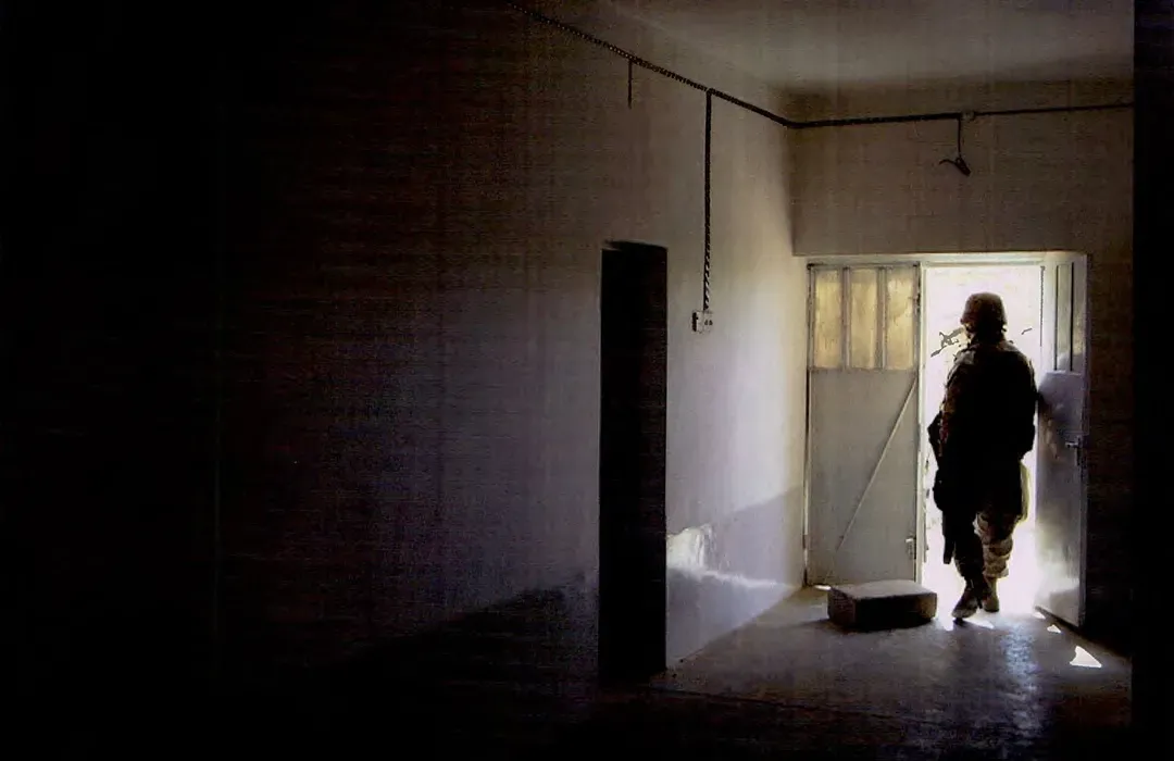 a soldier walks out of a darkened hallway with his back to the photographer