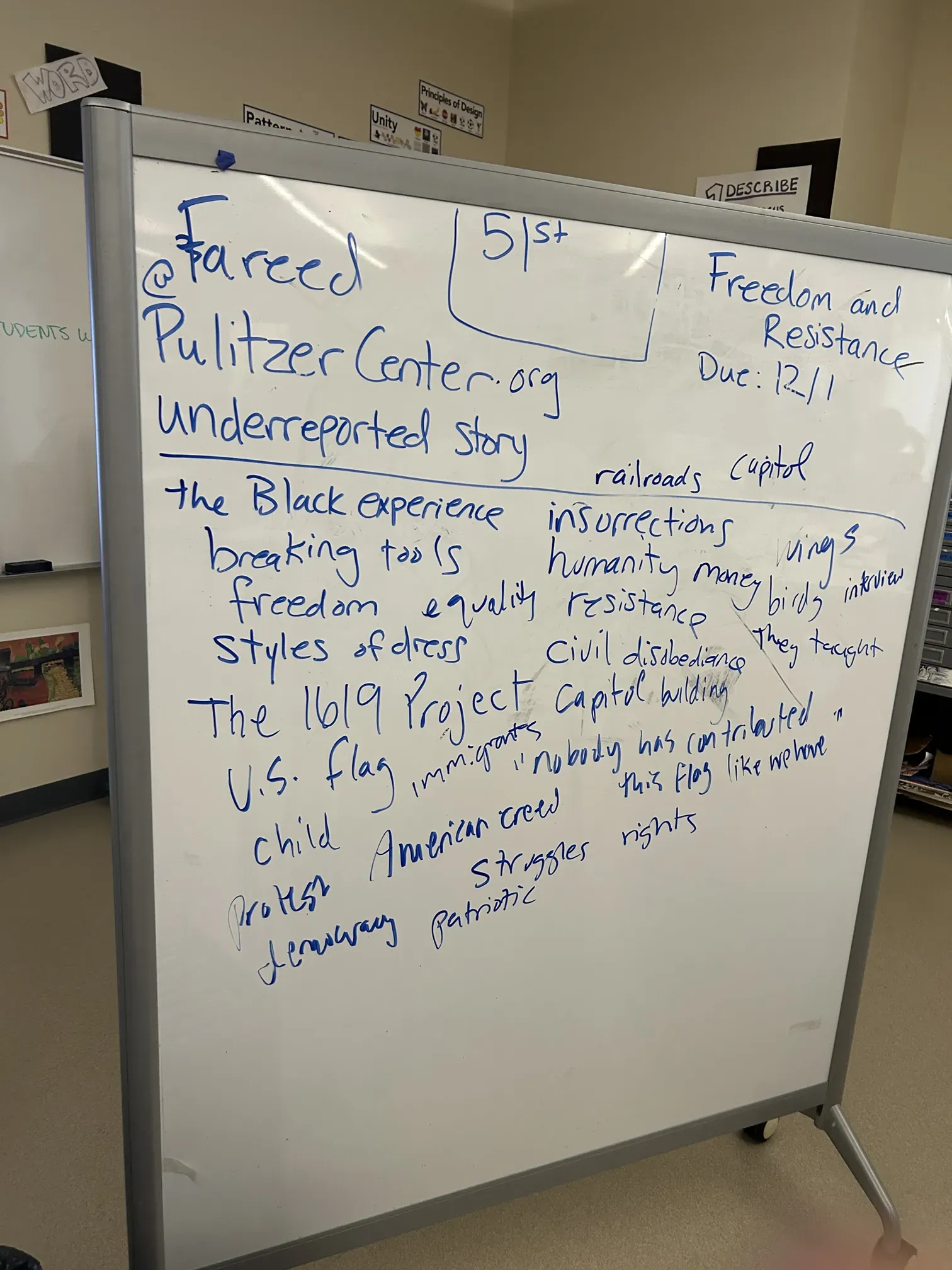 A whiteboard with a series of words that remind students of exhibition themes of 'freedom' and 'resistance.' words include 'struggles', 'patriotic', 'protest', 'democracy', 'humanity', and 'U.S. flag'.