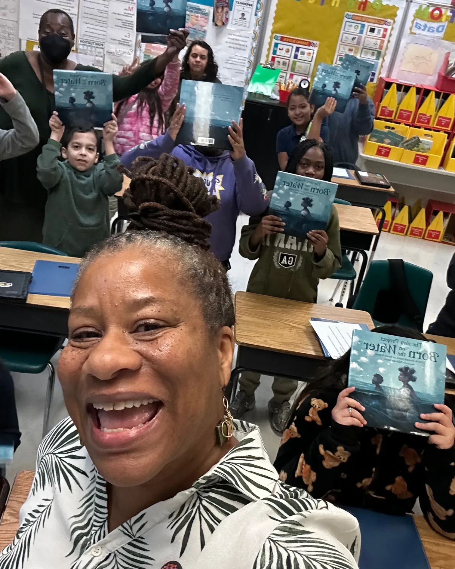Project Lead, Veronica Jones, takes a selfie with students holding up copies of Born On The Water in the classroom
