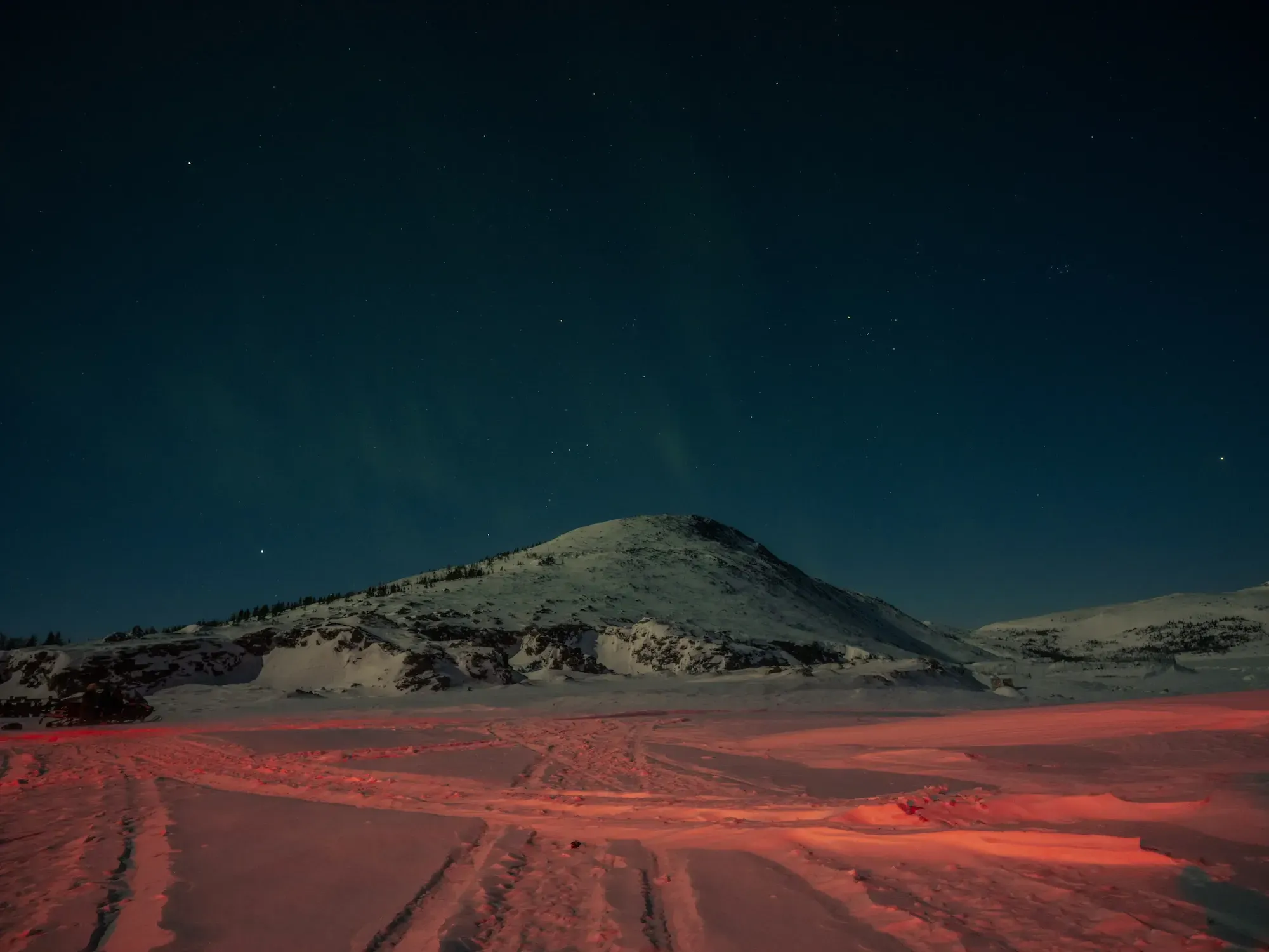 The aurora borealis can be seen in the clear winter sky and reflected as a scarlet glow on the ice on the outskirts of Nain, creating a colourful and surreal nightscape. Image by Johnny C.Y. Lam. Canada.