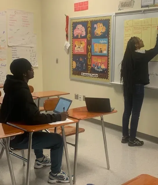 a student writes on the KWHL chart paper posted on the white board