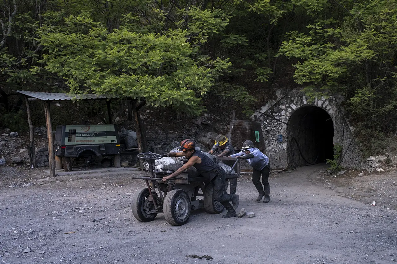 Three workers, straining, push a cart from a mine.