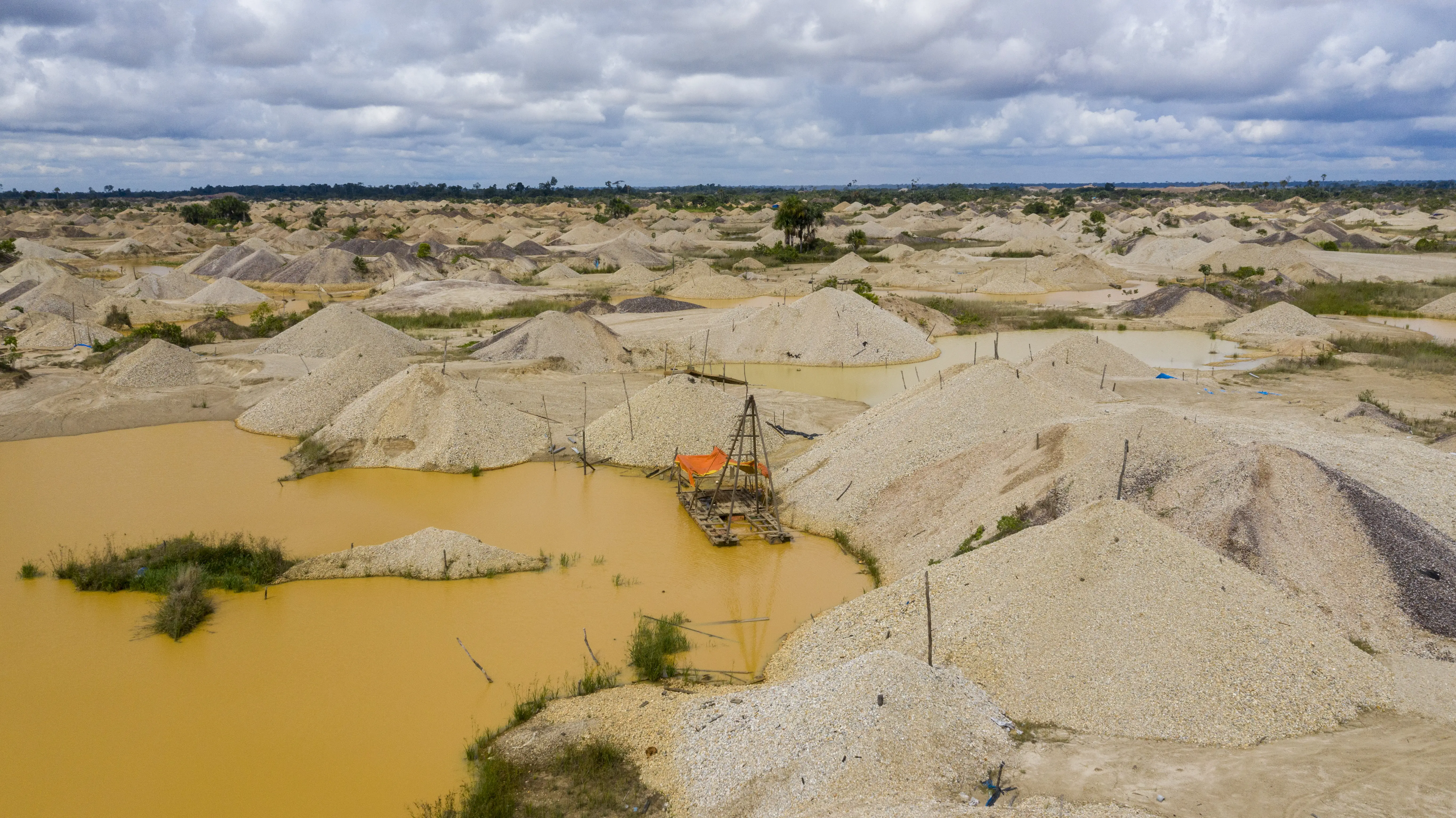 Mining rafts and equipment wait on embankments of silt and gravel around reddish runoff.