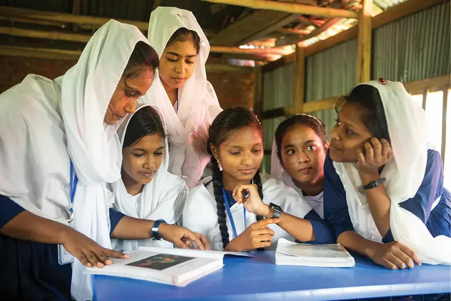 Six students crowd around a blue table looking at a textbook.